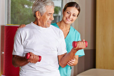physical therapist assisting a senior man exercising with dumbbells