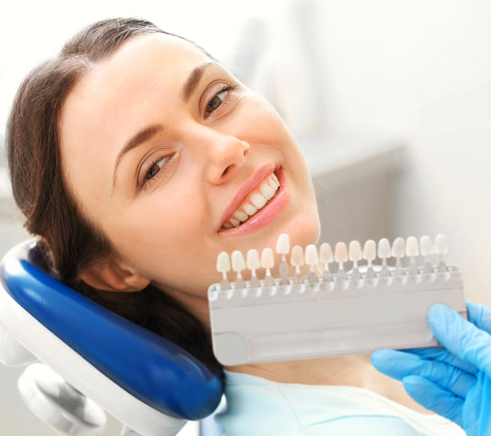 Dentist checking and selecting color of young woman's teeth
